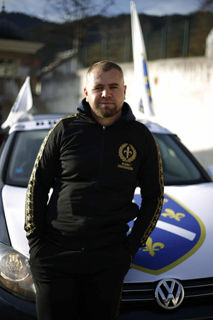 Covijek u trenerci Ljiljan ispred auta sa zastavom ljiljan na haubi