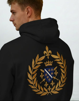 Osoba koja nosi crnu majicu s kapuljačom i zlatnim amblemom na leđima na običnoj pozadini
